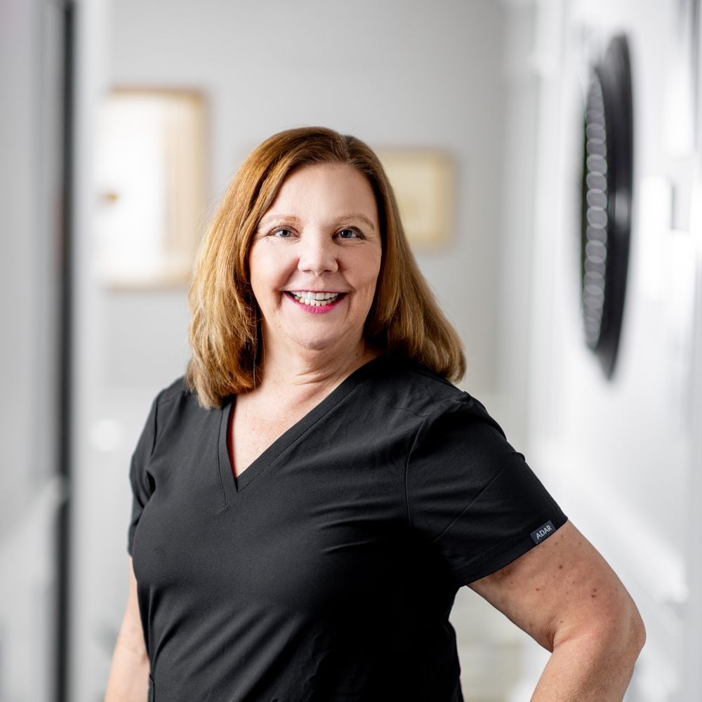 Smiling woman in black scrubs against light background.
