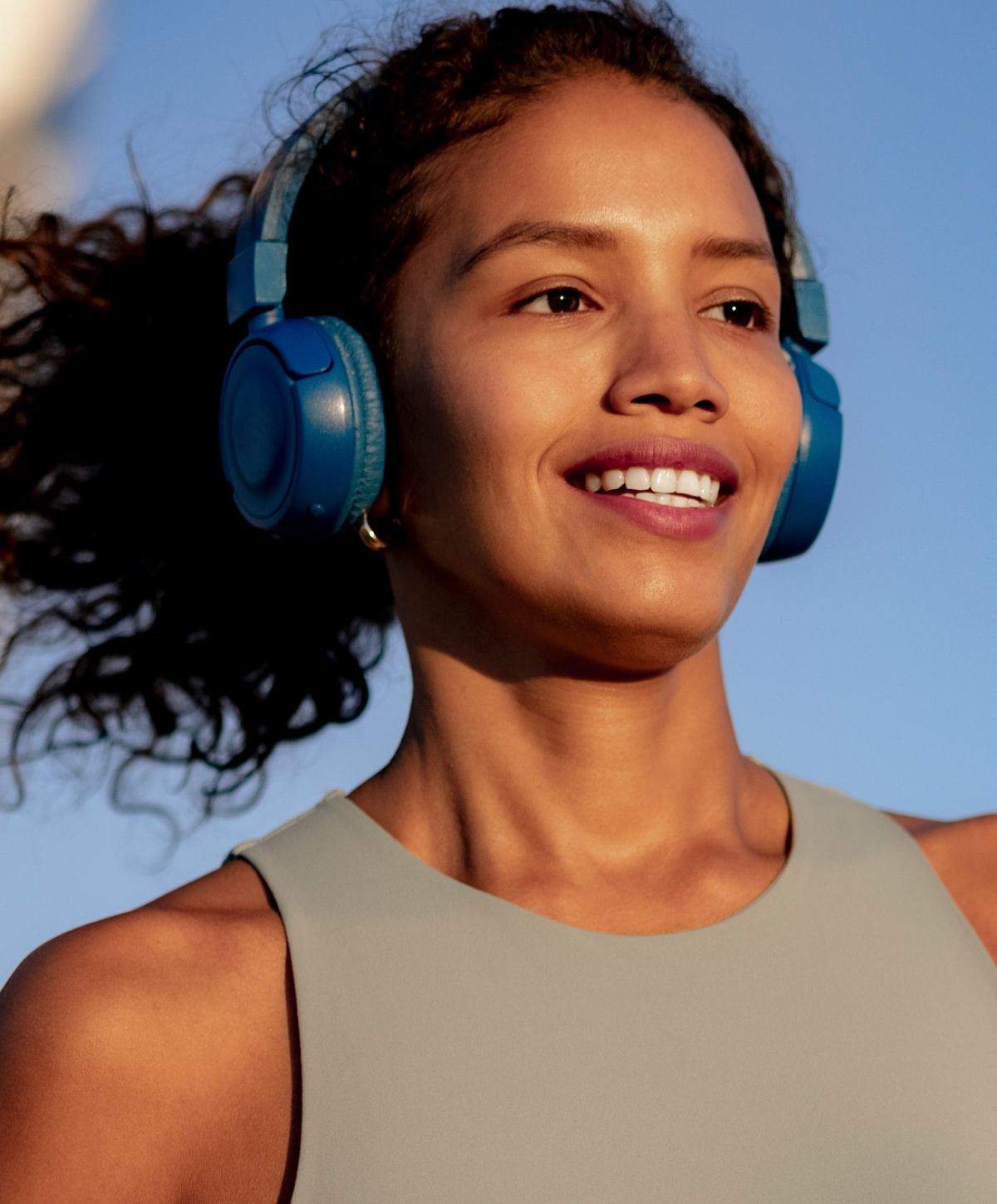 Smiling woman wearing blue headphones outdoors.